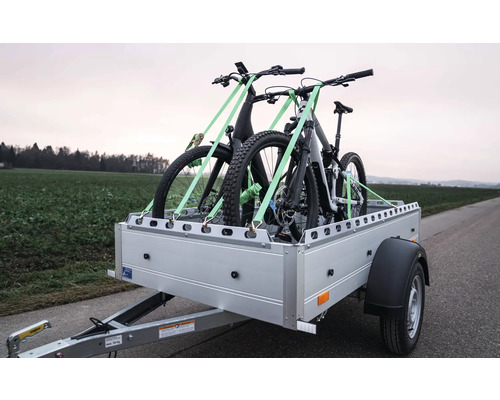 Pkw-Anhänger mit zwei Mountainbikes, die mit Spanngurten auf der Ladefläche für den Transport gesichert sind.