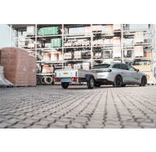 Auto mit einem Humbaur Anhänger auf einem Lagerplatz für Baumaterialien vor Regalen.