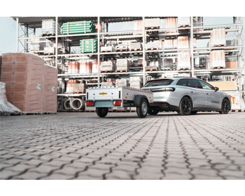 Auto mit einem Humbaur Anhänger auf einem Lagerplatz für Baumaterialien vor Regalen.