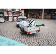 Beladener Humbaur Anhänger mit Dämmplatten, Schubkarre und Rohren, angekuppelt an ein Auto vor einem Baustofflager.