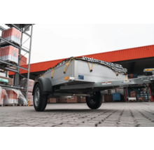 Einachsiger Anhänger für Autos mit silberner Ladefläche und schwarzem Ladungssicherungsnetz im Außenbereich eines Baumarktes.