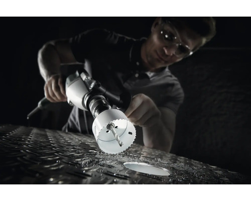 Ein Mann bohrt mit einer Lochsäge ein Loch in eine Metalloberfläche.