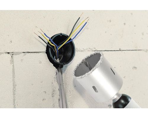 Mur avec trou de forage, câbles électriques et une scie cloche.