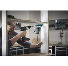 Un homme assemble une étagère avec une visseuse sans fil et un serre-joint à une main.