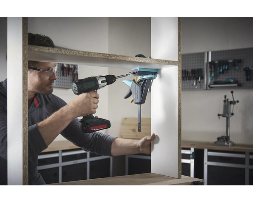 Un homme assemble une étagère avec une visseuse sans fil et un serre-joint à une main.