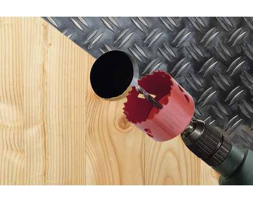 Une scie cloche perce un trou dans une planche de bois.