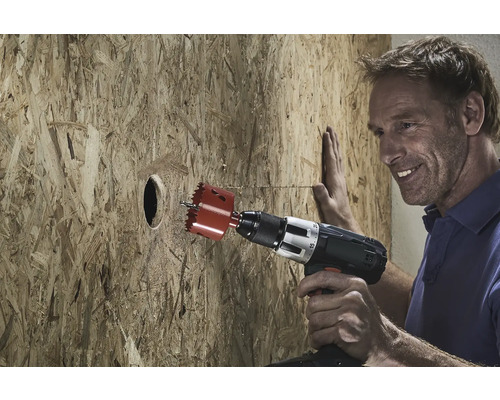 Un homme perce un trou avec une scie cloche dans une planche de bois