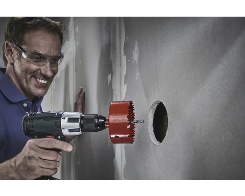 Un homme perce un trou dans un mur avec une scie trépan