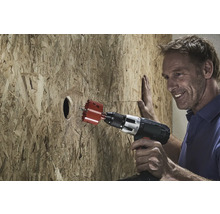 Un homme perce un trou dans une plaque de bois avec une scie cloche.