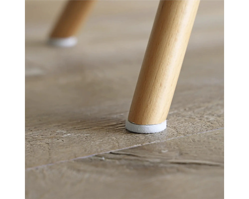 Vue détaillée d'un pied de chaise avec protection de sol sur un plancher en bois.
