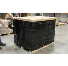 Une palette de cartons, emballée dans un film étirable noir, est sécurisée par une personne à l'aide d'un dérouleur manuel.