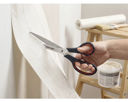 Une personne coupe du papier peint avec des ciseaux de la marque Rautner