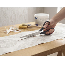 Une personne coupant un morceau de papier peint à motifs avec des ciseaux Rautner sur une table