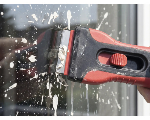 Grattoir à peinture en cours d'utilisation pour enlever les éclaboussures de peinture sur le verre.