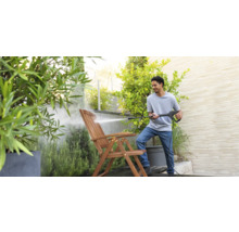 Mann reinigt Holzgartenstuhl mit Hochdruckreiniger im Garten