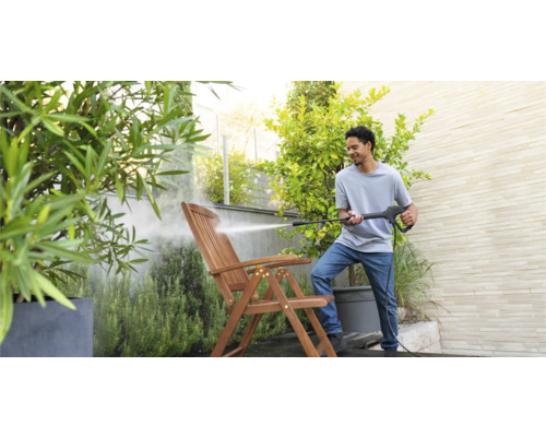 Mann reinigt Holzgartenstuhl mit Hochdruckreiniger im Garten