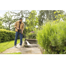 Ein Mann reinigt mit einem Hochdruckreiniger Steinstufen im Garten.