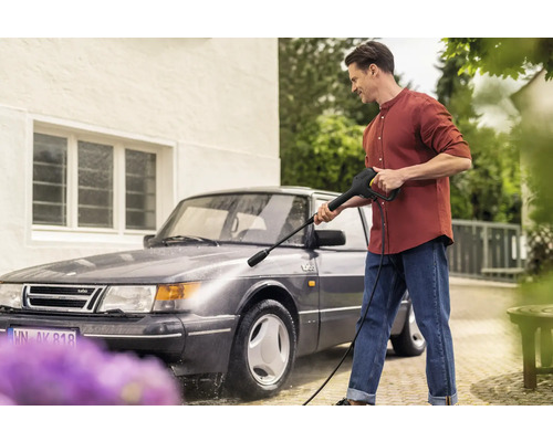 Mann reinigt Auto mit Hochdruckreiniger vor Haus