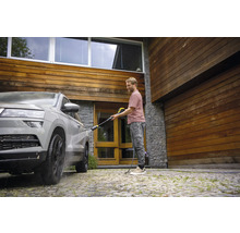 Mann reinigt Auto mit Hochdruckreiniger vor einem Haus mit Holzfassade