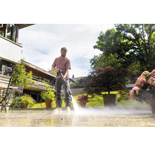 Ein Mann reinigt eine Terrasse mit einem Hochdruckreiniger in einem Garten.