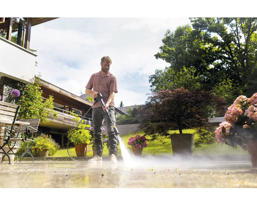 Ein Mann reinigt eine Terrasse mit einem Hochdruckreiniger in einem Garten.
