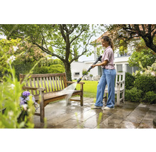 Eine Frau reinigt eine Holzbank mit einem Hochdruckreiniger im Garten.
