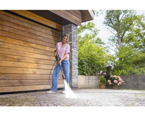 Frau reinigt Auffahrt mit Hochdruckreiniger vor Holzgarage