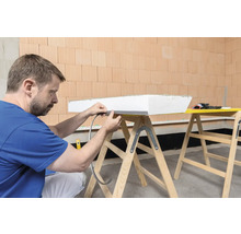 Mann befestigt Dichtband an einer Dämmplatte auf einem Holzbock