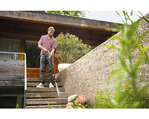 Ein Mann reinigt eine Treppe mit einem Hochdruckreiniger vor einem Wohnhaus.