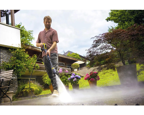 Mann reinigt mit einem Hochdruckreiniger eine Terrasse.