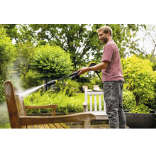 Mann reinigt Holzbank mit Hochdruckreiniger im Garten.