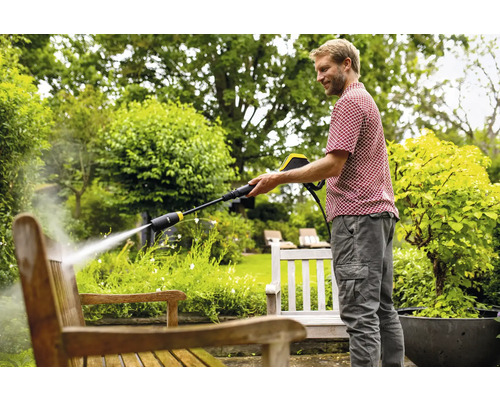Mann reinigt Holzbank mit Hochdruckreiniger im Garten.