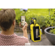 Eine Person hält ein Smartphone mit der Kärcher-App in der Hand, im Hintergrund ein Kärcher Hochdruckreiniger.