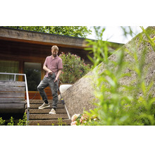 Mann reinigt eine Mauer mit einem Hochdruckreiniger auf einer Terrasse.