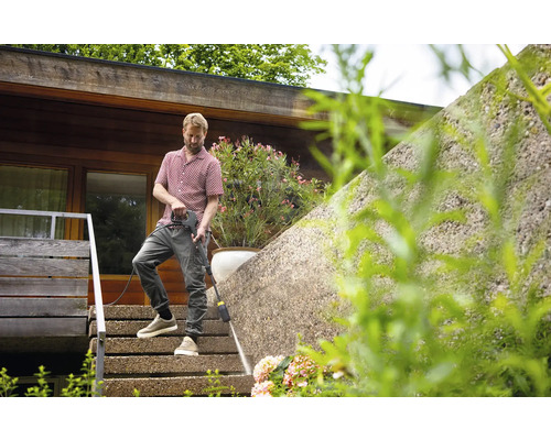 Mann reinigt eine Mauer mit einem Hochdruckreiniger auf einer Terrasse.
