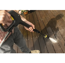 Eine Person reinigt eine Holzterrasse mit einem Hochdruckreiniger.