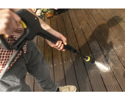 Eine Person reinigt eine Holzterrasse mit einem Hochdruckreiniger.