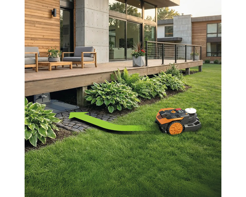 Mähroboter auf Rasen vor modernem Haus mit Ladestation unter der Terrasse