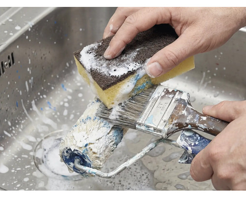 Nettoyage d'un rouleau à peinture et d'un pinceau avec une éponge dans l'évier.