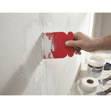 Un homme applique un couteau à mastic rouge sur un mur avec du ruban adhésif en fibre de verre