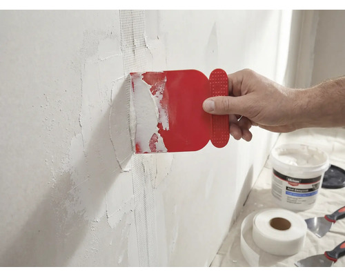Un homme applique un couteau à mastic rouge sur un mur avec du ruban adhésif en fibre de verre