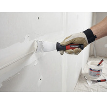 Un artisan enduit un mur avec un couteau à mastic et du mastic. Logo Rautner visible.