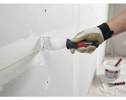 Un artisan enduit un mur avec un couteau à mastic et du mastic. Logo Rautner visible.