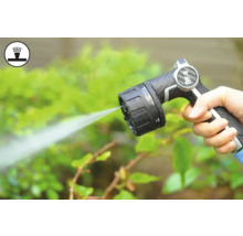 Hand hält Gartenschlauch-Spritzpistole beim Bewässern von Pflanzen