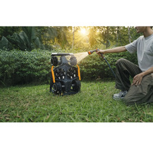 Mann reinigt einen Mähroboter mit einem Wasserschlauch im Garten.