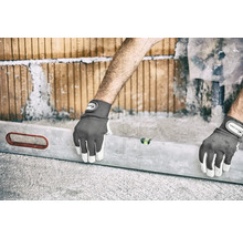 Eine Person, die mit einer Wasserwaage und Arbeitshandschuhen eine Wand aus Ziegelsteinen ausrichtet