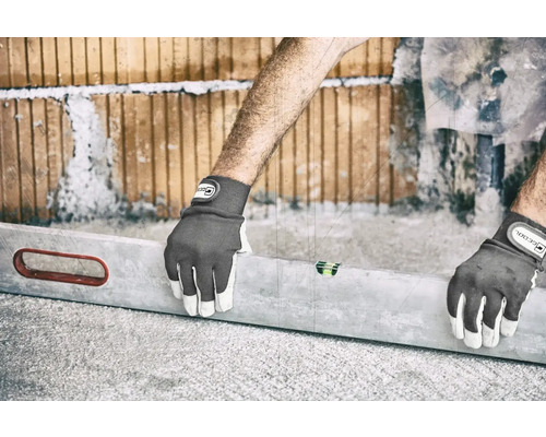 Eine Person, die mit einer Wasserwaage und Arbeitshandschuhen eine Wand aus Ziegelsteinen ausrichtet