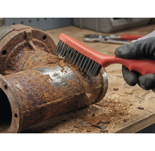 Une personne retire la rouille d'un tuyau métallique avec une brosse métallique.