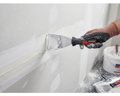 Eine Person spachtelt eine Wand mit einer Spachtelmasse und einem Spachtel von Rautner.