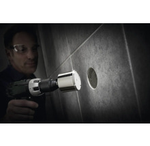 Un homme perce un trou dans un carreau avec une scie cloche diamantée.